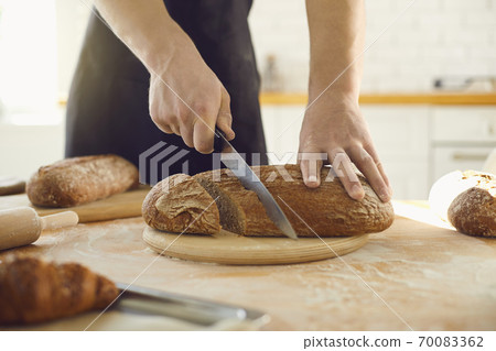 Hands cutting fresh homemade bread on a table in a bakery kitchen. Hands cutting fresh homemade bread on a table in a bakery kitchen. 70083362