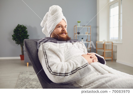 Funny strange fat bearded man in a bathrobe does spa treatments on his face rests in a room Funny strange fat bearded man in a bathrobe does spa treatments on his face rests in a room 70083970