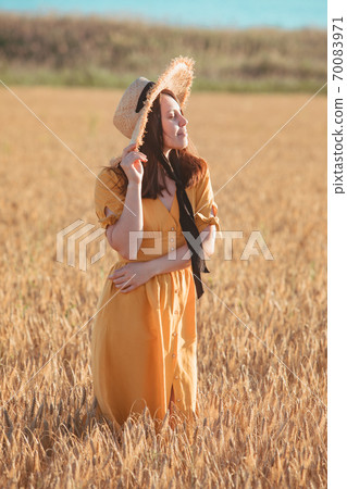 woman in yellow sundress walking by wheat field woman in yellow sundress walking by wheat field 70083971