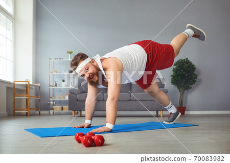 Funny fat man doing yoga exercises in the room. 70083982