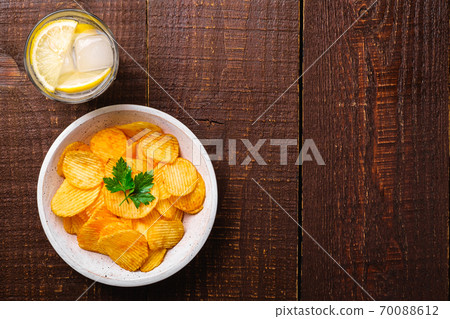 Fresh ice cold water drink with lemon near to fried potato chips with parsley leaf in wooden bowl on wood backdrop, top view copy space 70088612
