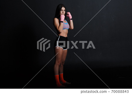 Sportsman muay thai woman boxer posing in training studio at black background. 70088843