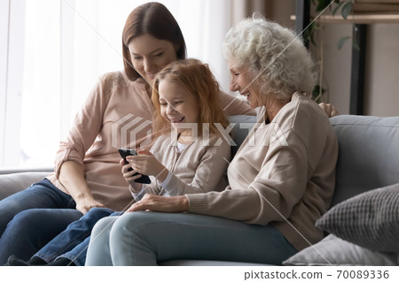 Happy little girl with mother and grandmother using smartphone Happy little girl with mother and grandmother using smartphone 70089336