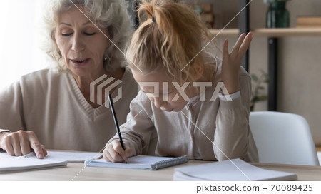 Close up mature grandmother helping unhappy little girl with homework 70089425