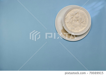 Some of the ingredients for the dough cooked in white plates. Flour yeast salt and baking powder. On a blue background. 70089915