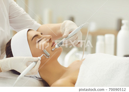 Woman receiving apparatus facial microcurrent treatment from therapist in beauty salon Woman receiving apparatus facial microcurrent treatment from therapist in beauty salon 70090512