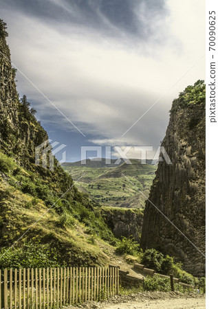 Hills and the medieval bridge over the Azat river in Garni gorge among the bushes and green grass against the blue sky covered with clouds Hills and the medieval bridge over the Azat river in Garni gorge among the bushes and green grass against the blue sky covered with clouds 70090625