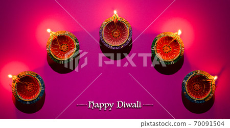 Happy Diwali - Clay Diya lamps lit during Dipavali, Hindu festival of lights celebration. Colorful traditional oil lamp diya on pink background 70091504