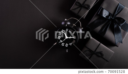 Top view of black gift box with Alarm clock on black paper background. Shopping concept Boxing day and Black Friday composition. 70091528
