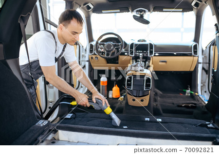 Worker cleans car trim with vacuum cleaner 70092821