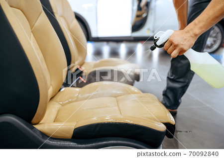 Worker with spray moisturizes car seat, detailing 70092840