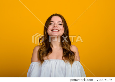 Dark-haired young woman with a smile and big suprised eyes posing on yellow background. Dark-haired young woman with a smile and big suprised eyes posing on yellow background. 70093086