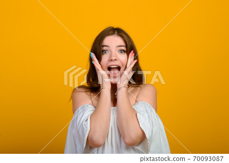 Dark-haired young woman with a smile and big suprised eyes posing on yellow background. 70093087