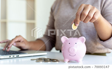 Young business women are saving money in a piggy bank and recording financial income-expenditures to prepare investments in real estate, Tax deduction and cost calculation concept. 70093147