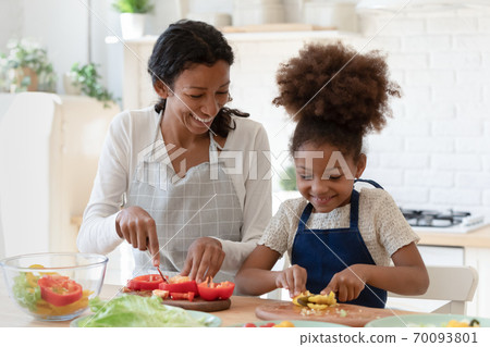 Happy young mixed race woman preparing food with daughter. 70093801