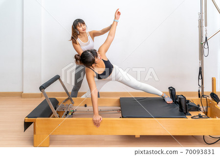 Young Asian woman working on pilates reformer machine during her health exercise Young Asian woman working on pilates reformer machine during her health exercise 70093831