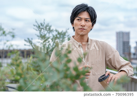 一個年輕人在建築物的屋頂上喝著電子煙在飲料上 一個年輕人在建築物的屋頂上喝著電子煙在飲料上 70096395
