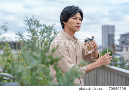 A young man smoking an e-cigarette over a drink on the roof of a building A young man smoking an e-cigarette over a drink on the roof of a building 70096396