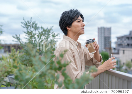 一個年輕人在建築物的屋頂上喝著電子煙在飲料上 一個年輕人在建築物的屋頂上喝著電子煙在飲料上 70096397