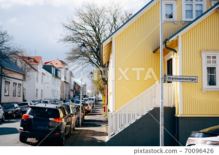 Yellow house with stairs and white railings, on the street in Reykjavik, the capital of Iceland. Cars parked along the road. 70096426