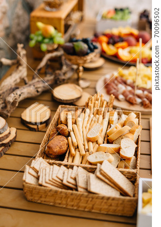 Wicker bread and cereal tray with sliced loaf, bread sticks and cookies on a wooden holiday table. Wicker bread and cereal tray with sliced loaf, bread sticks and cookies on a wooden holiday table. 70096502