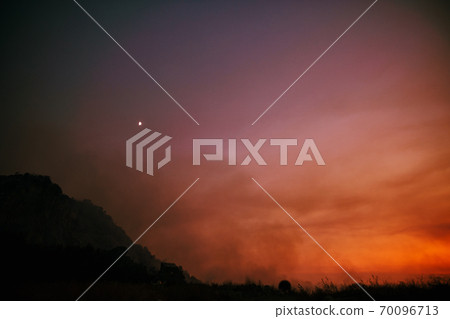 Forest fire in the mountains against the background of a fiery sunset sky. Forest fire in the mountains against the background of a fiery sunset sky. 70096713