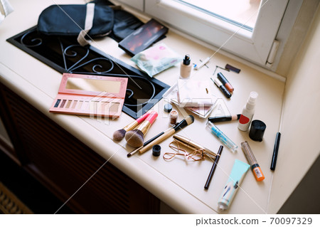 Makeup artist set. Eyeshadow palette, makeup brushes, mascara and eyelash curler on the windowsill by the window. 70097329