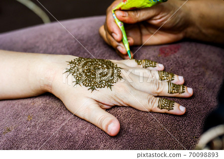 Mehendi artist paint henna on female hand, focus selective. Mehendi artist paint henna on female hand, focus selective. 70098893