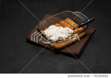 tiramisu dessert cooking - Traditional Italian Savoiardi ladyfingers Biscuits and cream in glass baking dish on dark concrete background tiramisu dessert cooking - Traditional Italian Savoiardi ladyfingers Biscuits and cream in glass baking dish on dark concrete background 70100882