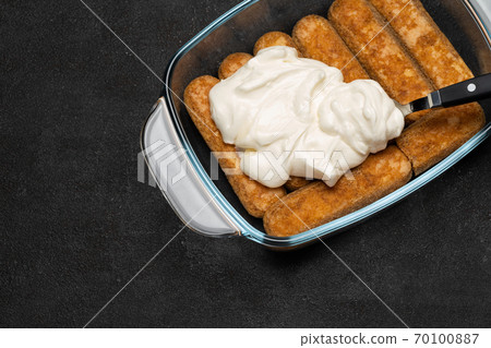 tiramisu dessert cooking - Traditional Italian Savoiardi ladyfingers Biscuits and cream in glass baking dish on dark concrete background tiramisu dessert cooking - Traditional Italian Savoiardi ladyfingers Biscuits and cream in glass baking dish on dark concrete background 70100887