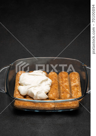 tiramisu dessert cooking - Traditional Italian Savoiardi ladyfingers Biscuits and cream in glass baking dish on dark concrete background tiramisu dessert cooking - Traditional Italian Savoiardi ladyfingers Biscuits and cream in glass baking dish on dark concrete background 70100894