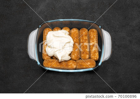tiramisu dessert cooking - Traditional Italian Savoiardi ladyfingers Biscuits and cream in glass baking dish on dark concrete background tiramisu dessert cooking - Traditional Italian Savoiardi ladyfingers Biscuits and cream in glass baking dish on dark concrete background 70100896