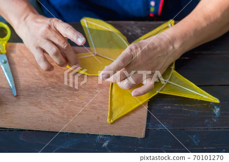Eldery woman making and build star-shaped kite or thai name Chula kite for sale at local market. Selective focus on .left hand finger.. 70101270