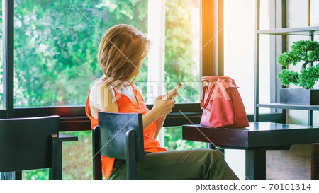 Asian female customer wear face mask using smartphone while sit in waiting social distance queue for take away drink in coffee shop. New normal lifestyle concept. Selective focus on hand. Asian female customer wear face mask using smartphone while sit in waiting social distance queue for take away drink in coffee shop. New normal lifestyle concept. Selective focus on hand. 70101314