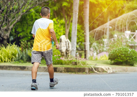 Back view portrait of a Asian elderly man in fitness wear walking and jogging for good health in public park. Senior jogger in nature.  Older Man enjoying Peaceful nature. Healthcare concept. 70101357