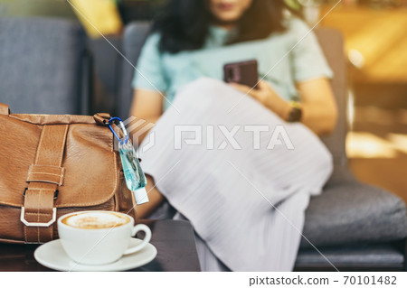 Mini alcohol gel bottle to kill Corona Virus(Covid-19) hang on a brown leather shoulder bag with hot coffee on table in cafe.New normal lifestyle.Health care concept.Selective focus on alcohol gel 70101482