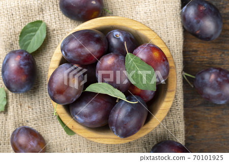 Ripe plums and leaves in a wooden bowl on the table. 70101925