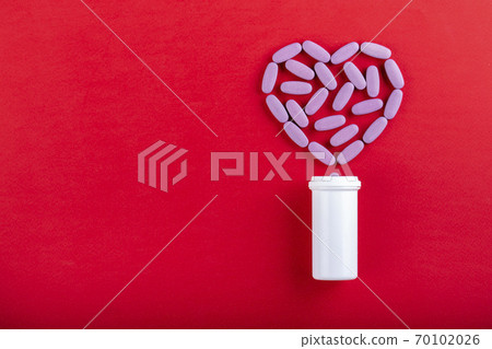 Tablets and bottle on red background top view. The tablets are laid out in the shape of a heart. Medical medicine. Space for text. Medicine creative concepts. Tablets and bottle on red background top view. The tablets are laid out in the shape of a heart. Medical medicine. Space for text. Medicine creative concepts. 70102026