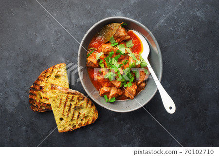 Slow cooked pork with vegetables, carrots, onions and ripe tomatoes with sweet peas and bay leaves in a plate. View from above. Comfortable homemade food 70102710