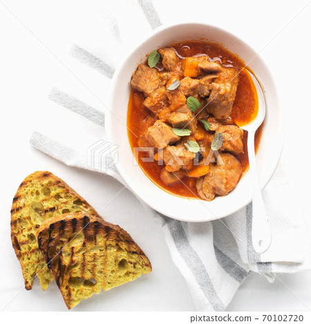 Slow cooked pork with vegetables, carrots, onions and ripe tomatoes with sweet peas and bay leaves in a plate. View from above. Comfortable homemade food 70102720