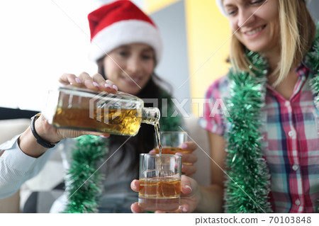 Women in red santa claus hats pour alcohol into glass with ice close-up 70103848