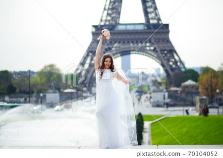 Beautiful bride in rich wedding dress whirls on the square before the Eiffel Tower 70104052