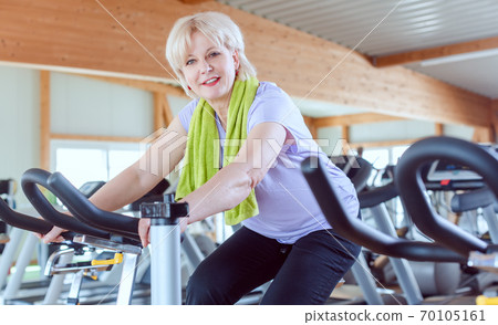 Senior woman exercising for better fitness on a bike in the gym Senior woman exercising for better fitness on a bike in the gym 70105161