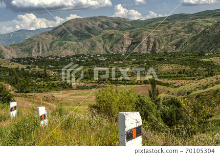 The village by the road is located in the mountains of the Gegham range against the blue sky covered with clouds in Armenia 70105304