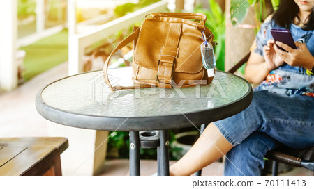 Mini portable alcohol gel bottle to kill Corona Virus(Covid-19) hang on a brown leather shoulder bag on table in garden. New normal lifestyle. Health care concept. Selective focus on alcohol gel Mini portable alcohol gel bottle to kill Corona Virus(Covid-19) hang on a brown leather shoulder bag on table in garden. New normal lifestyle. Health care concept. Selective focus on alcohol gel 70111413