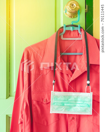 New surgical mask to prevent the spread of Corona Virus(COVID-19) hanging with red shirt on a hanger on a door knob in front of bedroom. New normal lifestyle before go to work concept. 70111445