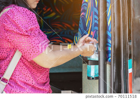 Hands of female passenger pressed an alcohol gel bottle to prevent the spread of Corona Virus(COVID-19) before traveling on a double-decker bus.Travel safely on public transport. New normal lifestyle. 70111518