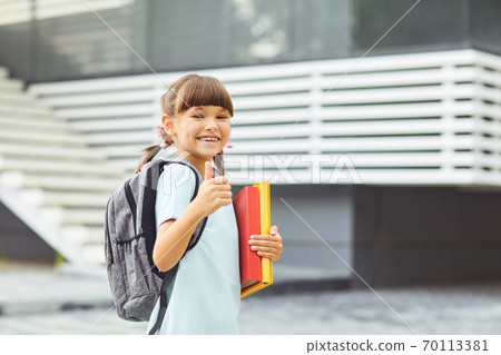 Smiling girl schoolgirl with a backpack in hand goes to school. 70113381
