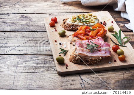 Wholegrain bread sandwiches with cream cheese, bacon and olives canned peppers with tomato on wooden background. Copy space. Wholegrain bread sandwiches with cream cheese, bacon and olives canned peppers with tomato on wooden background. Copy space. 70114439