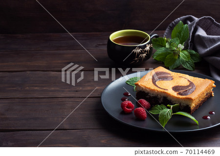 A piece of double-layer cake on a plate of chocolate brownies and curd cheesecake with raspberries. Dark background copy space 70114469